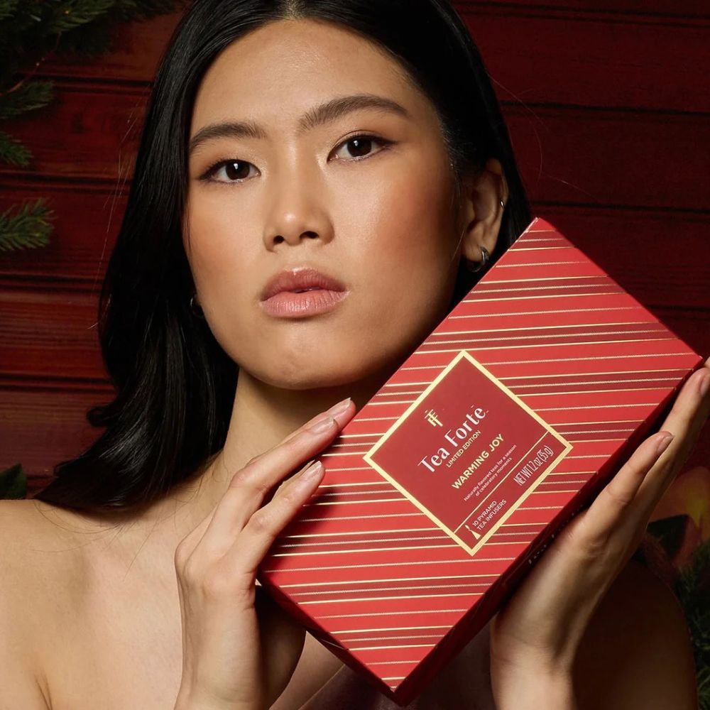 Woman holding a red striped Tea Forte Warming Joy Petite Presentation Box beside her face
