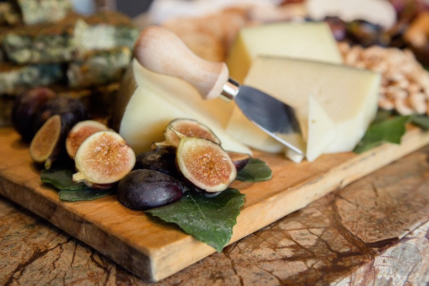 Beautiful charcuterie board with figs cheeses and greenery on wooden display board