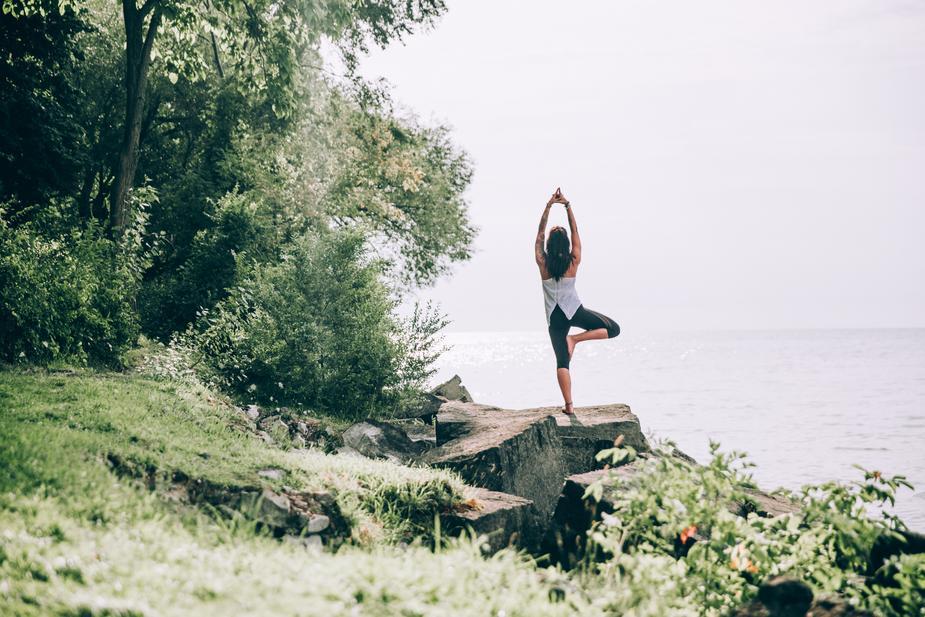 Woman doing tree yoga pose on peaceful cliff overlooking ocean