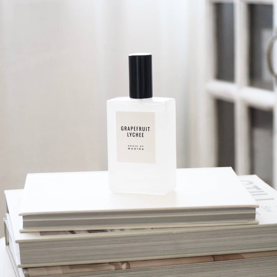 House of Mahina Grapefruit Lychee Room + Linen Mist, frosted glass bottle with black cap on a stack of white books