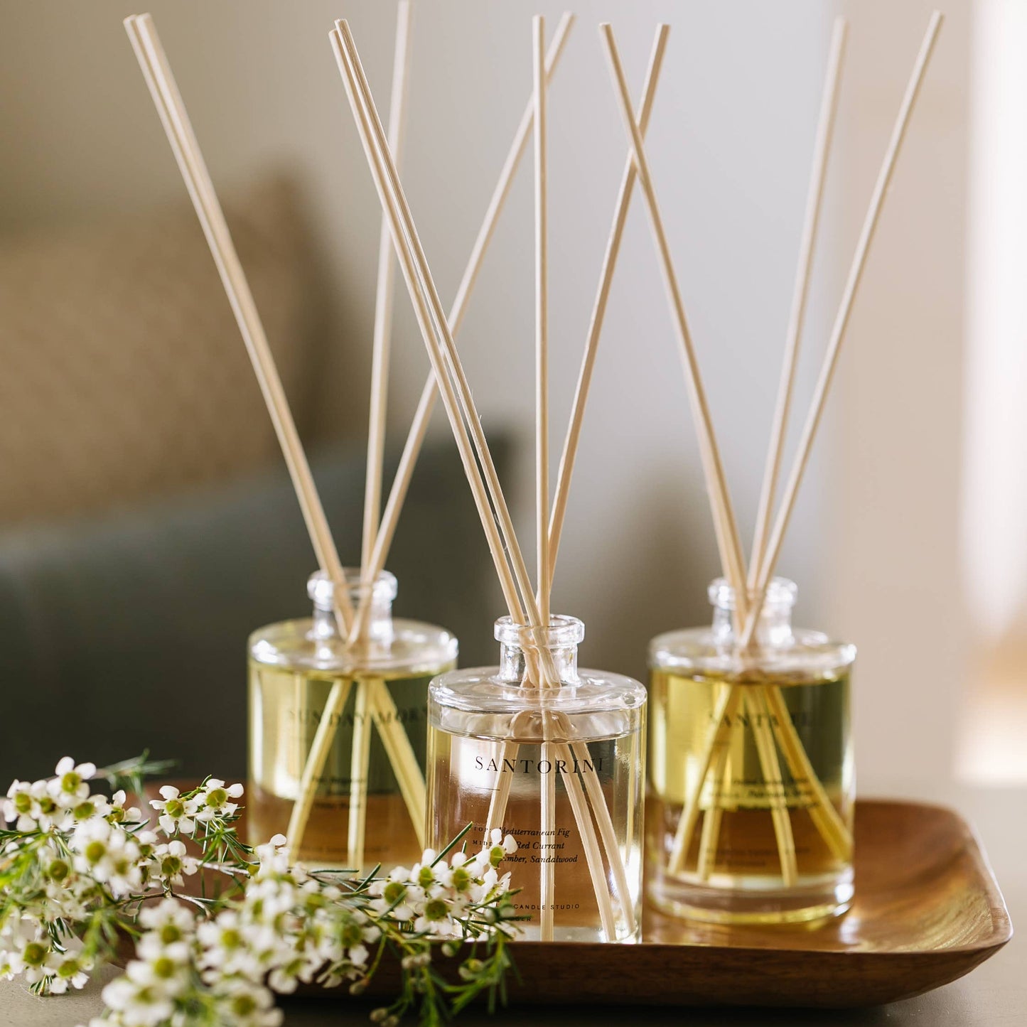 Three Brooklyn Candle Studio reed diffusers on a wooden tray with flowers