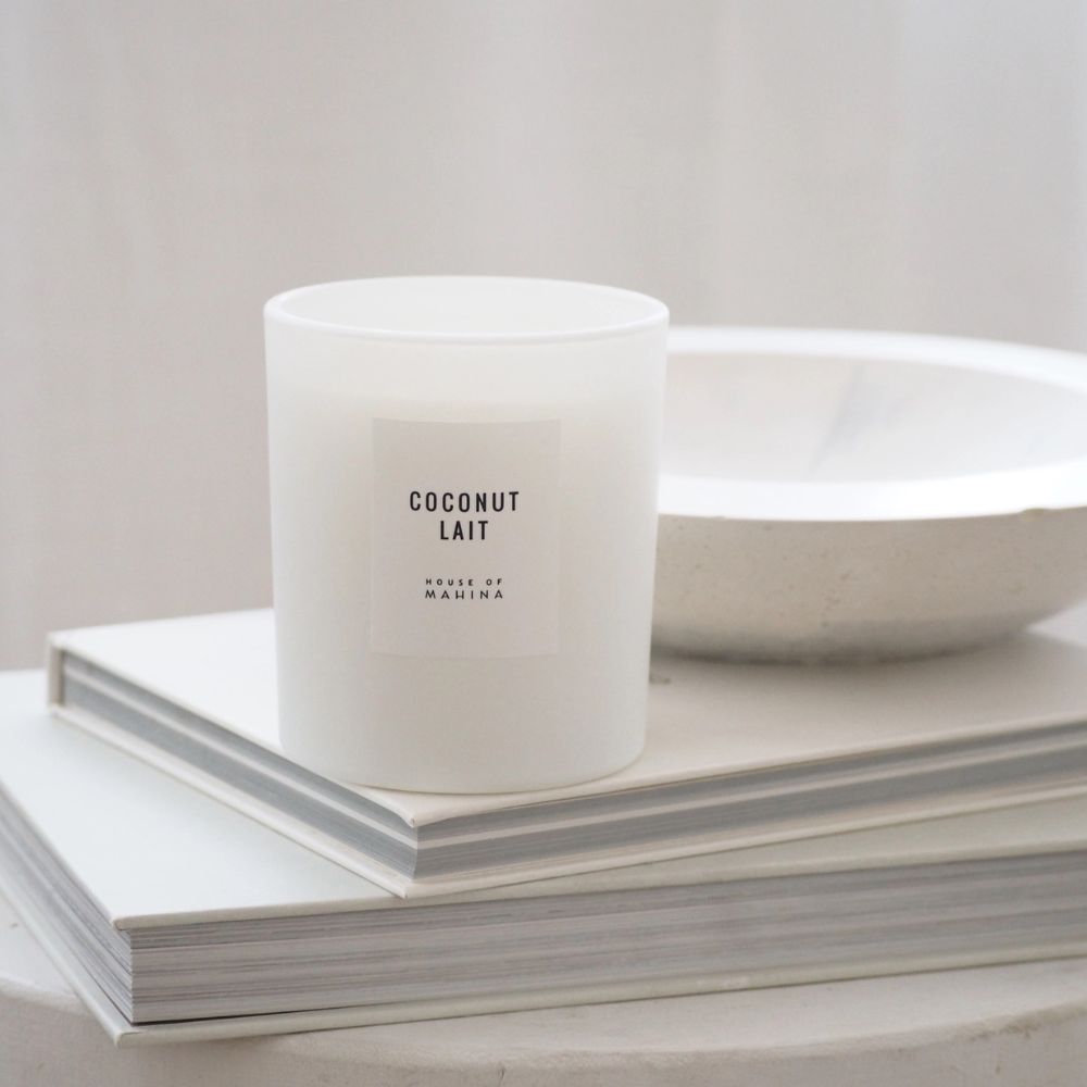 Coconut Lait candle on stack of white books with white round bowl in background