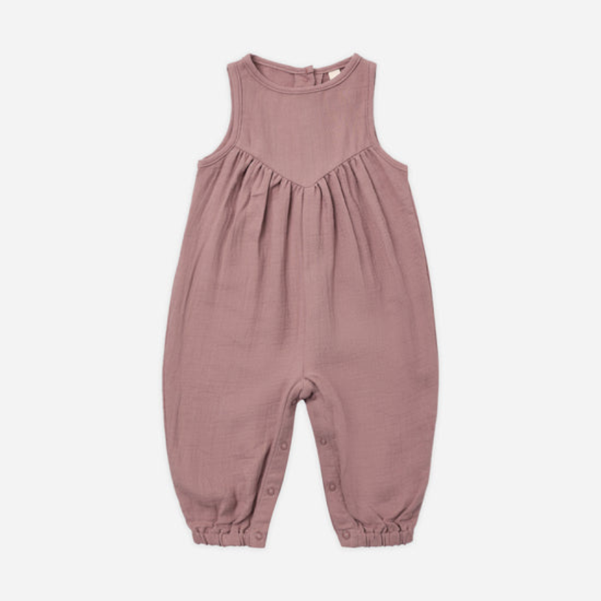 A sleeveless baby jumpsuit in a dusty rose pink color, made of textured cotton fabric with a gathered chest and elasticized leg cuffs, shown flat on a light gray background.