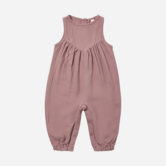 A sleeveless baby jumpsuit in a dusty rose pink color, made of textured cotton fabric with a gathered chest and elasticized leg cuffs, shown flat on a light gray background.