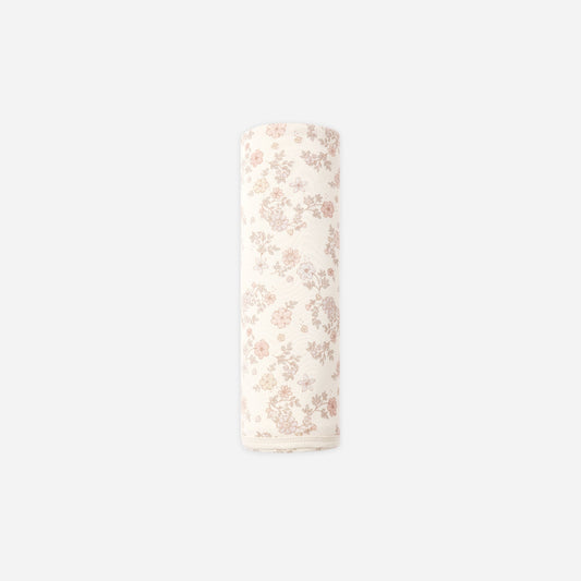 A rolled-up cream-colored fabric item, likely a muslin cloth or baby blanket, featuring a delicate pink floral pattern, shown against a solid light gray background.