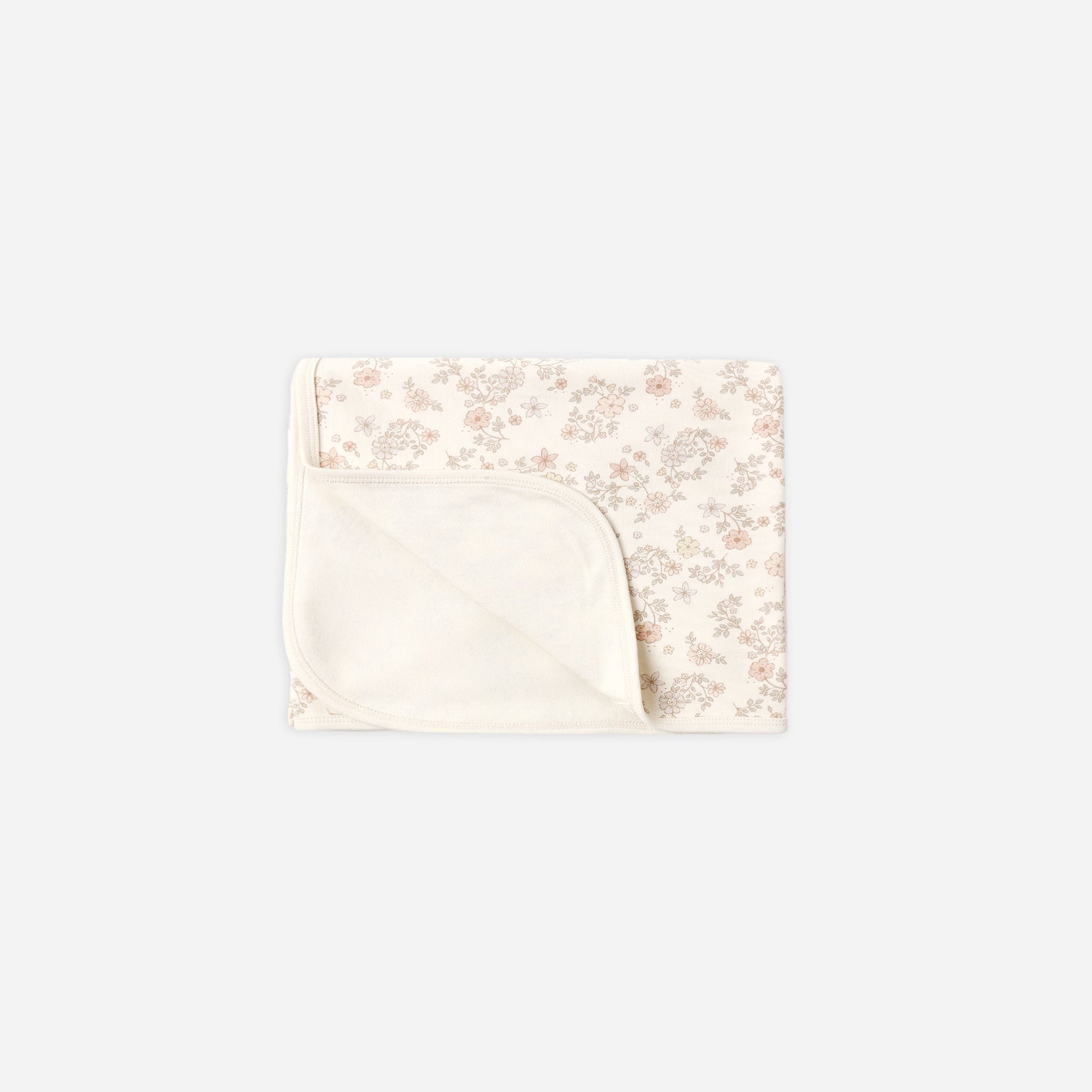 A folded baby blanket with a soft cream-colored solid fabric underside and a top half featuring a delicate, small-scale floral pattern in muted pink and beige on an off-white background.