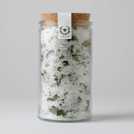 Glass jar with cork lid containing a sea salt and dried eucalyptus leaves.