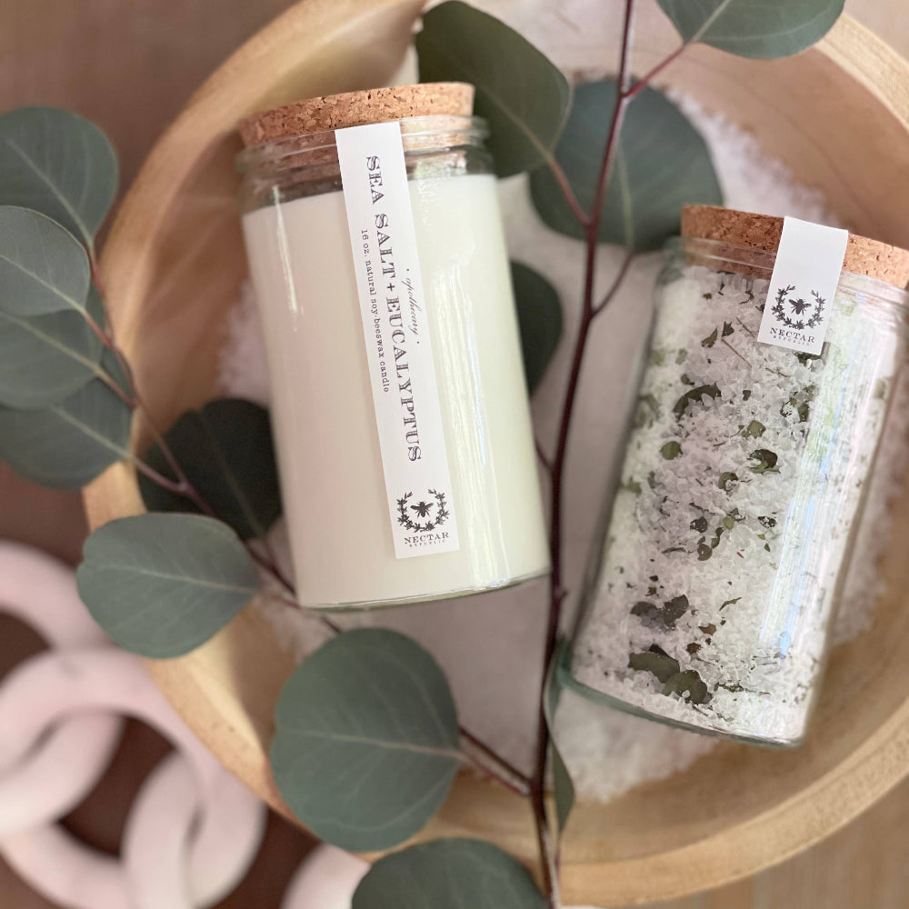 Nectar Republic Sea Salt and Eucalyptus candle and bath salts duo on wooden surface with greenery