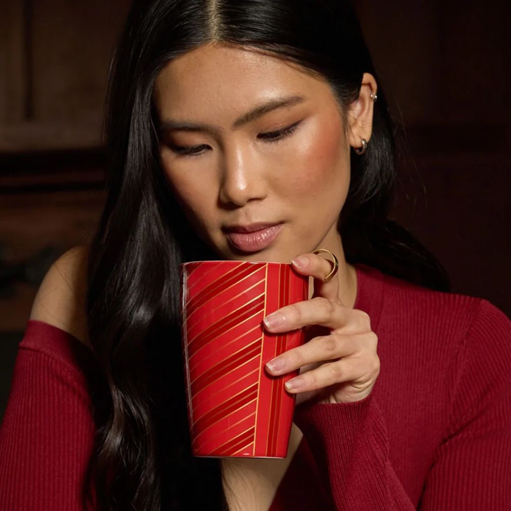 Woman in a red sweater sipping from a red striped Tea Forte Warming Joy Kati cup