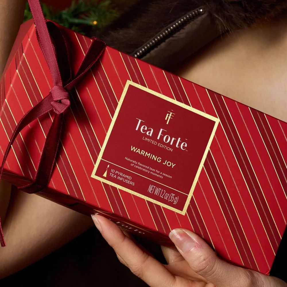 Hands holding a red striped Tea Forte Warming Joy gift box tied with a red ribbon