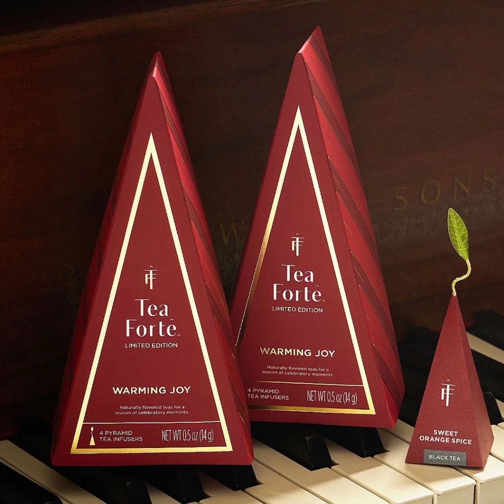 Red and gold Tea Forte Warming Joy tree boxes in three sizes standing on piano keys
