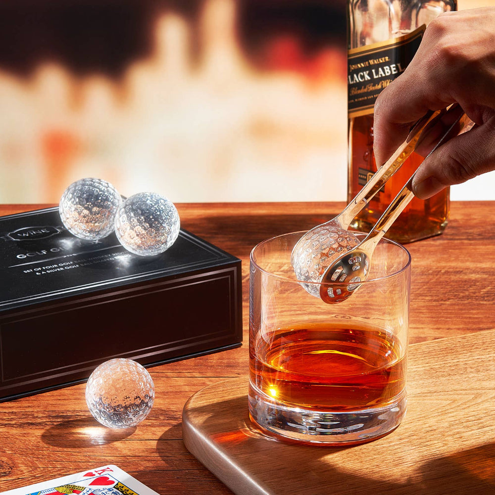 Glass of whiskey with ice cubes, bottle of Johnnie Walker Black Label, and ice cube tongs on a wooden table.