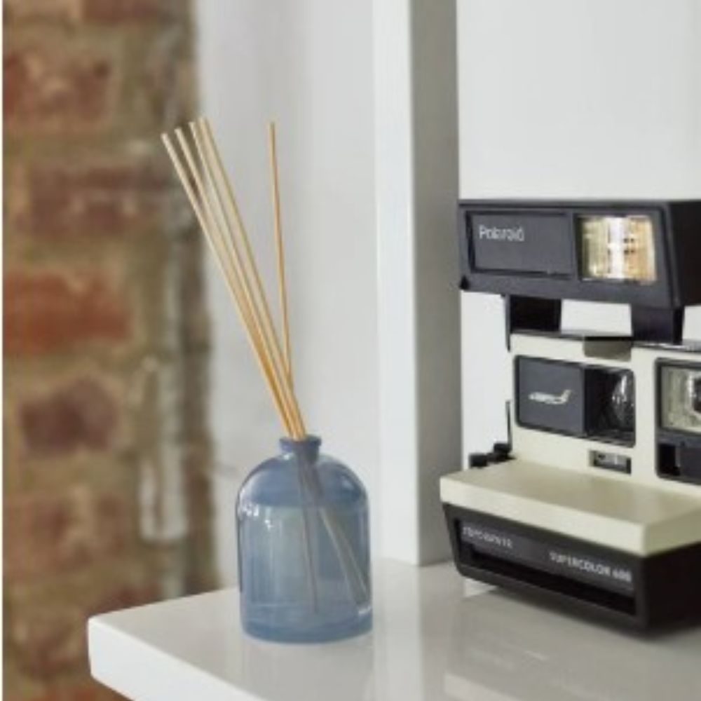 Light blue Wild Fig reed diffuser bottle on countertop with polaroid camera in background